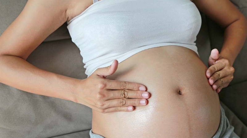 Một phụ nữ mang thai đang nhẹ nhàng chạm vào bụng mình, thể hiện sự kết nối với thai nhi, trong bối cảnh yên bình